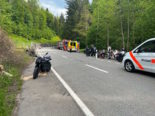 Motorrad steht im Wald links am Strassenrand, rechts weitere Motorräder und Fahrer, ein Polizeiauto und ein Ambulanzwagen